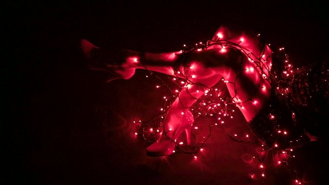 Sexy female legs on the ground in a dark room tangled in red lights wearing high heels and a short black skirt as she is kicking her legs out, with copy space.