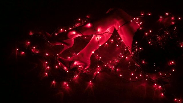 Sexy female legs on the ground in a dark room tangled in red lights wearing high heels and a short black skirt