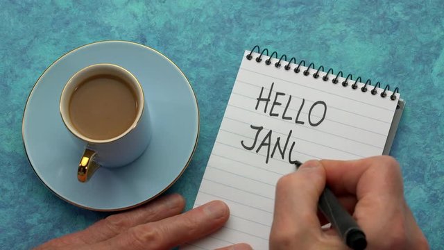 Hello January - a man hand writing a note with a black marker in a notebook, overhead view with a cup of coffee