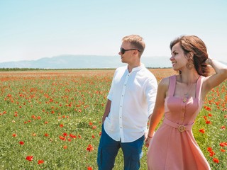 Brunette girl in pink dress leads on poppy field blonde man in white cotton shirt in Provence in France, Valensol