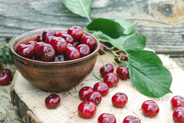 Red cherry in a bowl and green leaves on old wooden boards. Juicy delicious fruit.
