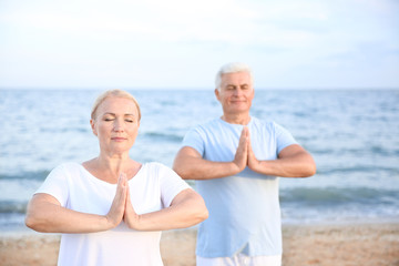 Mature couple practicing yoga at sea resort