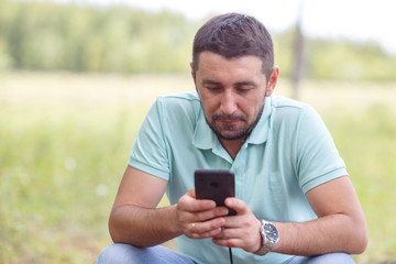 bearded man in light green shirt with phone outdoors on summer day