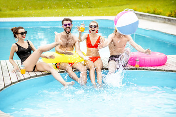 Group of a happy friends having fun, playing with inflatable balls and rings on the water pool outdoors during the summer time