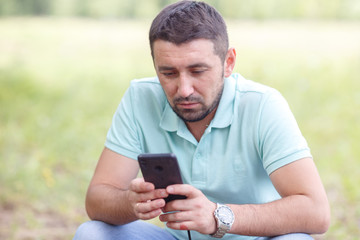 bearded man in light green shirt with phone outdoors on summer day