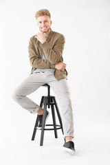 Stylish young man sitting on stool against white background