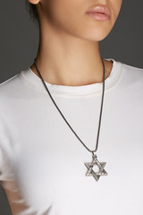 Cropped top and bottom photo of a woman with a necklace on her neck. The model on a gray background is dressed in a white tee-shirt. You can see Star of David pendant with engraved intricate patterns 