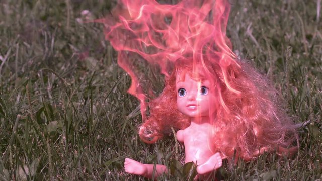 Burning baby doll sitting in grass slow motion