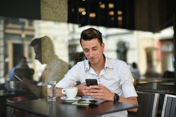 Young fashion man / hipster drinking espresso coffee in the city cafe during lunch time and working on tablet computer