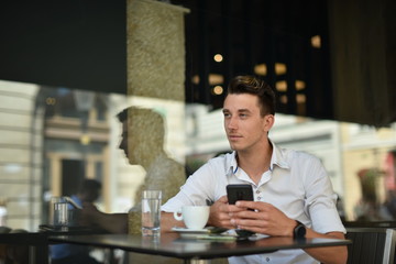 Young fashion man / hipster drinking espresso coffee in the city cafe during lunch time and working on tablet computer