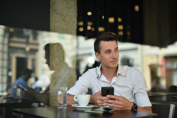 Young fashion man / hipster drinking espresso coffee in the city cafe during lunch time and working on tablet computer