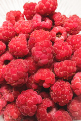 Close-up ripe juicy and delicious raspberry in a plastic transparent dish on a light background. Saturated healthy food