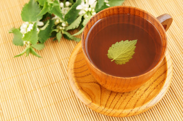 Wooden cup of nettle tea on bamboo mat