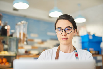 Barista wearing glasses and working on the laptop.