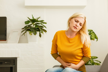 girl having period is sitting on sofa and feeling much of painful on her stomach and twist her...