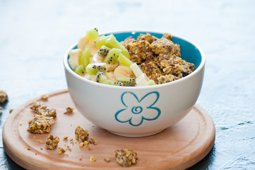 Healthy breakfast of granola, kiwi, banana and yogurt in a bowl on a wooden tray. Fitness diet for weight loss