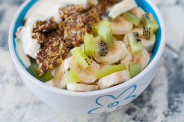 Granola, kiwi, banana and Greek yogurt in bowl, a plate on a gray concrete background, close-up view from the top. Fitness diet for weight loss and proper nutrition
