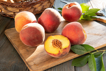 Sweet ripe juicy fruit, peaches with green leaves on dark wooden background on cutting Board