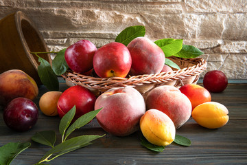 Sweet ripe juicy fruits, peaches, plums, quince with green leaves in a wicker basket on a dark wooden background on a cutting Board