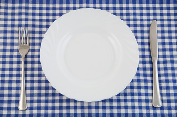 Top view of white plate, fork and knife on tablecloth