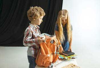 Boy and girl preparing for school after a long summer break. Back to school. Little caucasian models packing a bag together on studio background. Childhood, education, holidays or homework concept.