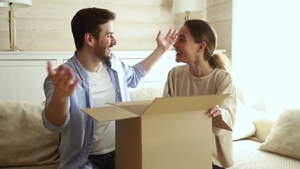 Happy excited couple customers open cardboard box sitting on sofa