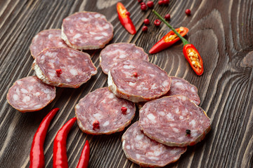 Sliced smoked salami with chilly pepper on wooden background.