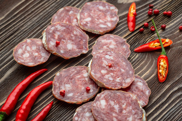 Sliced smoked salami with chilly pepper on wooden background.