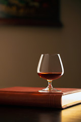 Glass of Cognac on book and dark interior  background 