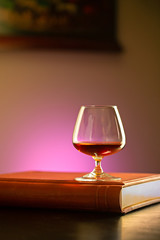 Glass of Cognac on book and dark interior  background 