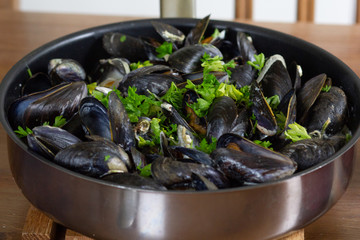 Cooked mussels in wine and cream with greens and onion served in skillet