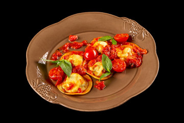 Plate of italian ravioli with spinach served with basil and tomato sauce isolated at black background.