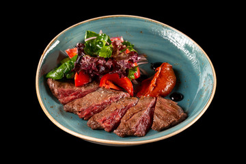 Bbq skirt steak served with griiled vegetables on a plate isolated at black background.