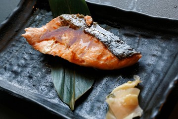 Selective focus of grilled mackerel steak with teriyaki sauce and pickled ginger on bamboo leaf in...