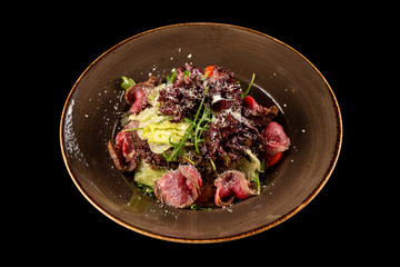 Plate of roast beef salad  with fresh tomatoes, salad mix with ginger sauce and parmesan cheese isolated at black background.