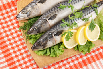 Mackerel fish with greens, lemon and cutting board on tablecloth