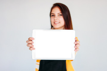 Naklejka premium Beautiful smiling brunette girl teenager in yellow t-shirt holding tablet in hands, isolated on white background, mockup
