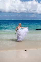 Fototapeta na wymiar young beautiful woman in a long white bride dress runs along the edge of the blue sea