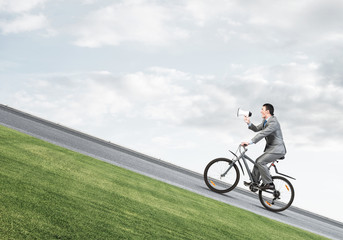 Obraz premium Businessman with megaphone in hand on bike