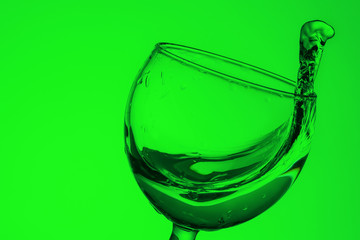 Splash of water in a glass on neon green background. Close up.