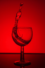 Splash of water in a glass on red background. Close up.