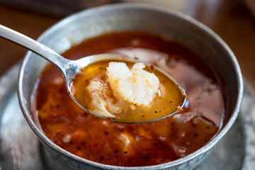 Kelle Paca soup in a bowl / plate with spoon and lemon on wooden table. Traditional soup of Gaziantep, Turkey. Famous Turkish cuisine fresh food foams. Veal meat ingredients in regional soup. Khash