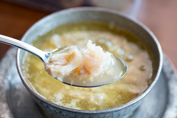 Kelle Paca soup in a bowl / plate with spoon and lemon on wooden table. Traditional soup of Gaziantep, Turkey. Famous Turkish cuisine fresh food foams. Veal meat ingredients in regional soup. Khash