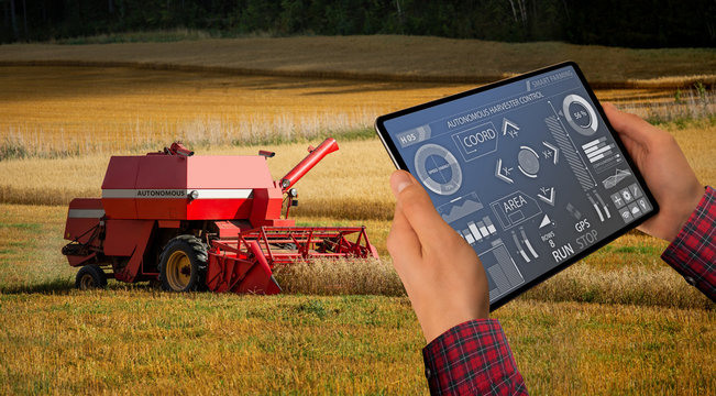 Farmer uses a digital tablet to control autonomous harvester. Smart farming concept.	
