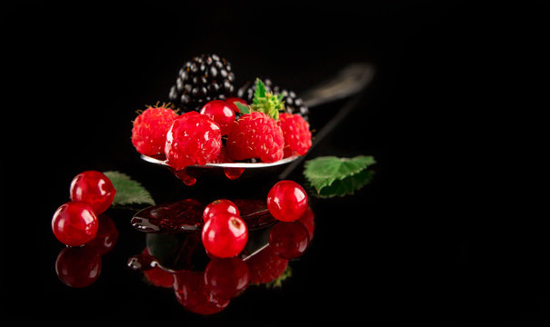 Blackberries , red currants, raspberries decorated with mint on a dark background with reflection.