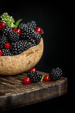 Blackberries , red currants in a coconut Cup on a dark background and a wooden Board.