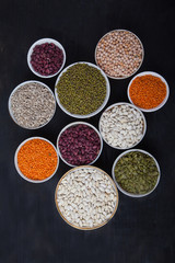 Red and white beans, green and red lentils, sunflower and pumpkin  in cups on a black background. superfood