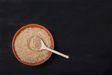 unpolished rice with a wooden spoon in a clay bowl on a black background. superfood