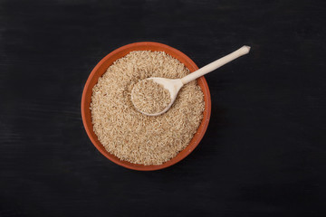 unpolished rice with a wooden spoon in a clay bowl on a black background. superfood