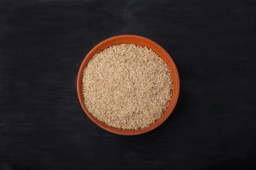 unpolished rice in earthenware on black background. superfood